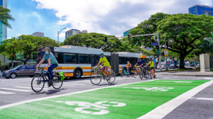 Image of a crosswalk with bicyclists crossing and City bus in the background.